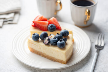 Cheesecake slice with blueberries and strawberries topping, served with cup of espresso coffee