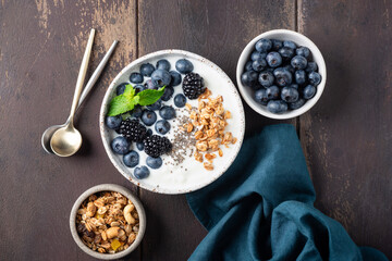 Healthy meal with greek yogurt, blueberries, blackberries, chia seeds and granola in bowl. Top view