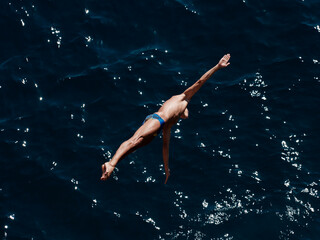 a professional male diver is jumping off a cliff into the sea