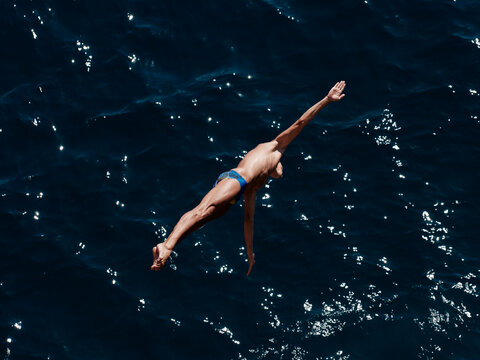 a professional male diver is jumping off a cliff into the sea