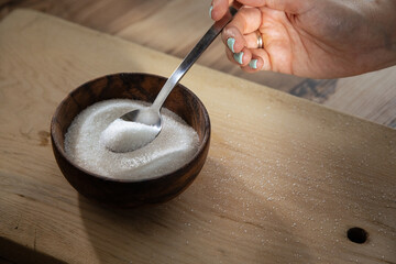 Granulated sugar filled in wooden bowl and hand with a spoon. Close up view of white sugar