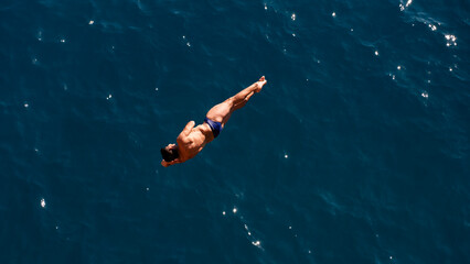 a professional male diver is jumping off a cliff into the sea
