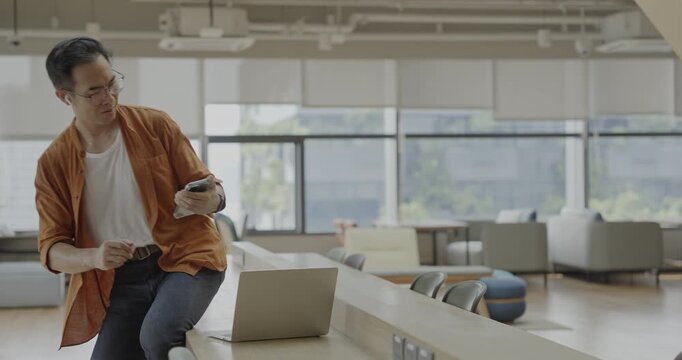 Senior Asian businessman wearing headset celebrates success during online meeting in modern co-working space. Remote work and business communication concept