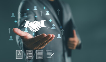 Businessman showing handshake icon with employee growth symbols and contract documents, representing partnership, recruitment, collaboration, HR strategy and human resource development in business.