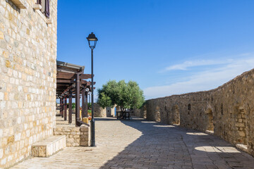 Sunlit stone courtyard in Ulcinj’s Old Town, Montenegro, with an olive tree framed by medieval walls. The scene captures the historic charm of the Adriatic coast under a clear blue sky.