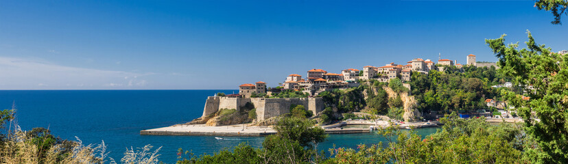 Panoramic view of Ulcinj’s historic Old Town with medieval stone walls, red-tiled roofs, and Adriatic Sea backdrop on a bright summer day.