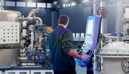 Engineer operates industrial control panel in a modern factory with metal tanks and pipelines, focused on automation, manufacturing, machinery, and industrial process control.