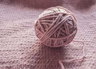 A pretty soft pink yarn ball resting gently on a beautifully knitted fabric surface