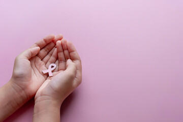 A hands holding a small pink awareness ribbon. Copy space for text. Breast cancer awareness concept.