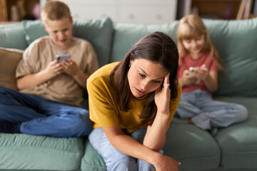 Single mother feeling worried while her kids are using cell  phones at home and ignoring her.