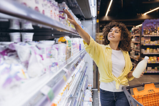 Woman choosing dairy products in supermarket refrigerator shelf