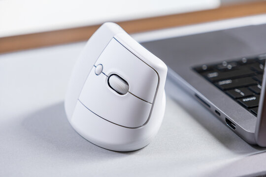 White ergonomic vertical mouse stands beside a laptop, promoting wrist comfort and enhanced productivity for efficient digital work in modern office and home environments
