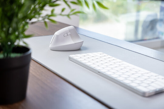 White ergonomic vertical mouse and minimalist keyboard on a grey desk mat, enhancing comfort, health, and productivity for a modern home office