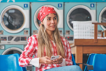 Customer using phone while waiting for laundry, sitting on blue plastic chairs in a laundromat