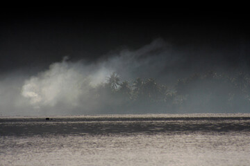 Dramatic smoke drifts across a mysterious coastal tropical landscape