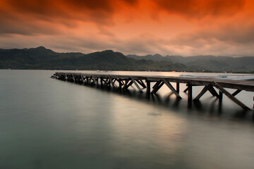 Obraz premium Serene pier extends into calm water at dramatic sunset