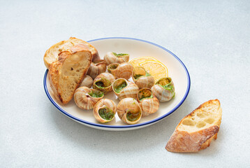 Escargots de bourgogne snails cooked with garlic butter, parsley and lemon wedges served on plate with toasted slices of baguette, a traditional french dish