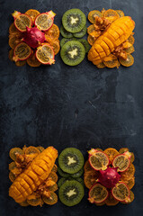 Geometric arrangement of tropical sliced fruits &ndash; dragon fruit, kiwi, mango, passionfruit &ndash; luxury minimal flat lay on dark slate background, premium healthy food concept, vivid colors