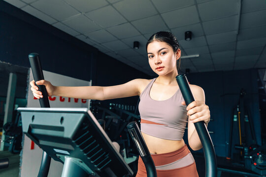 Close-up of cute Asian young woman exercise on elliptical cross trainer in fit sportswear, girl practice working out training for health.