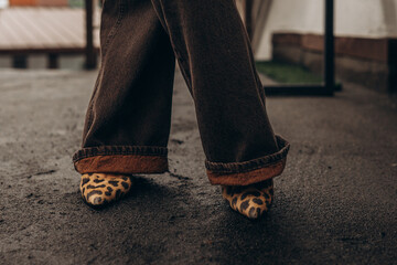 Legs of a woman in shoes. Close-up of fashionable leopard print shoes paired with wide-legged trousers on a city street
