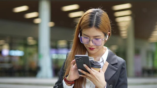  Close-up of Asian businesswoman using mobile phone, texting and cheating on her smartphone while outside office.