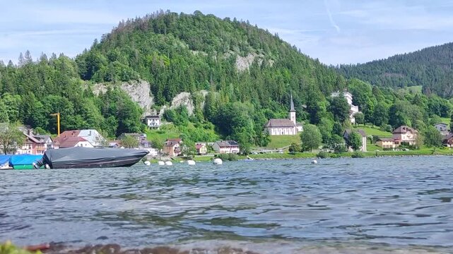 A picturesque view of a lakeside village Le Lieu , Switzerland  surrounded by verdant hills, illustrating the harmony between human habitation and nature's beauty in a tranquil setting, us01