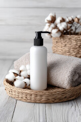 Clean and minimalist lotion pump bottle is placed on woven basket alongside soft towel and cotton flowers, creating serene and inviting atmosphere for skincare routines