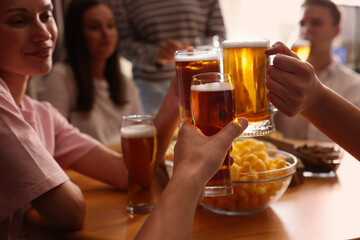 Group of happy friends clinking glasses of beer at table indoors, selective focus