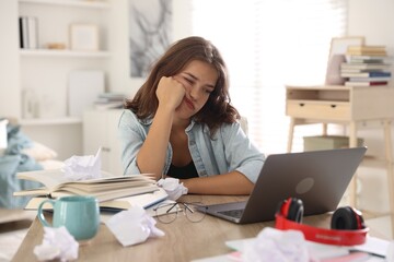 Tired student preparing for exam at table indoors