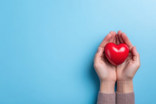 top view of hands holding red heart in concept healthcare, wellbeing, organ donation, and insurance life. World Heart Day World Health Day National Organ Donor Day. On a blue background