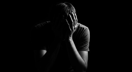 Dramatic black and white portrait of a man in despair, his face hidden in his hands, symbolizing loneliness, depression, and mental anguish.