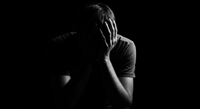 Dramatic black and white portrait of a man in despair, his face hidden in his hands, symbolizing loneliness, depression, and mental anguish.