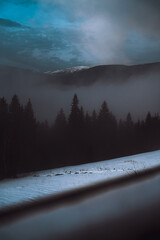 Winter mountains in the haze, blue sky and a strip of snow like a path into the silence of the forest.