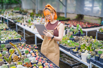 Young Asian Woman Working in Greenhouse Farm as Eco Business Owner with Tablet in Cactus Shop