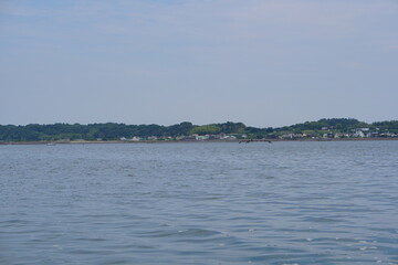 静かな湖面の向こうに広がる対岸の集落と緑豊かな森を望む風景。水辺の穏やかさと自然の豊かさを感じさせる、旅行や観光素材として活用できる爽やかな景観写真。