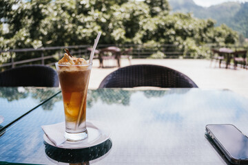 Refreshing iced coffee topped with ice cream and cinnamon resting on a table in an outdoor cafe, with a smartphone and wicker chairs in the background