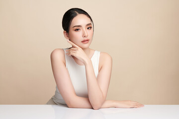 Naklejka premium A beautiful young Asian woman with clean, fresh skin against a beige background. Skincare, facial treatment, cosmetology, beauty, and spa. An elegant portrait of an Asian woman.