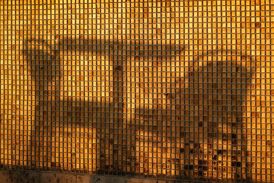 The shadow of a cafe table and two chairs on a glittering golden mosaic wall in the morning sun. This warm, abstract texture evokes the peaceful, inviting atmosphere of a summer holiday breakfast