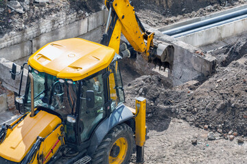 Excavator at construction site performs earthworks on a hot sunny day, excavator working against dug water main background, excavator operation close-up.