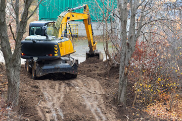 Fototapeta premium The excavator is digging the soil at a new construction site, the excavator is digging the soil in an area with trees, excavator operation in construction.