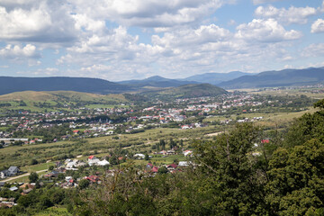 panoramic view from neamt fortress over a picturesque valley in romania with a town nestled among rolling green hills, surrounded by a lush green landscape