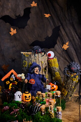 halloween, forest, clearing, witch sits on stump in his cozy shelter with spiders, ghost, eye, pumpkins and conjures over jars of potions on the eve of All Saints Day, selective focus