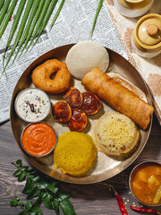 Traditional South Indian breakfast platter served in a brass plate with popular dishes including idli, dosa, medu vada, upma, kesari bath, chutneys, and sambar.