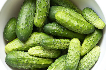 Fresh green cucumbers in white bowl top view. Organic vegetables with textured skin and natural color. Healthy raw food ingredient for salad or pickling. Seasonal harvest and vegetarian diet concept.