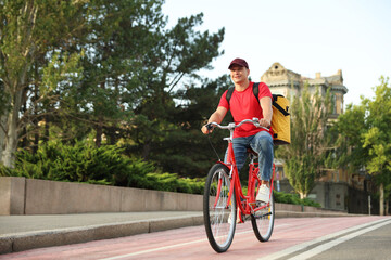 Obraz premium Courier with thermo bag riding bicycle outdoors, space for text. Food delivery service