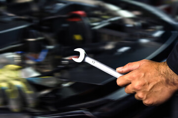 Car repair close up, mechanic hand holding open-end wrench in engine bay, blurred workshop background
