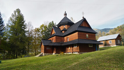 A historic wooden Orthodox church stands on a green hill in the Carpathian Mountains, embodying traditional Ukrainian folk architecture and spiritual heritage.