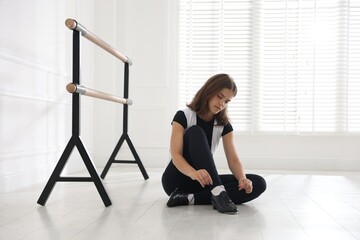 Teenage girl tying shoelace of tap shoe indoors