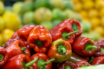 Fresh red bell peppers piled in bulk at a market, with blurred yellow and green peppers in the background adding vibrant color contrast.
