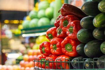 Fresh red bell peppers and cucumbers neatly arranged at a market stall, highlighting vibrant...